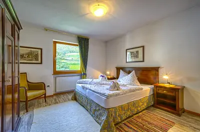 a bedroom with a bed and a chair and a window at Hotel & Residenz Traubenheim in Nalles