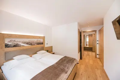a bedroom with a large bed with white sheets at Apartments Sosaslong in Selva di Val Gardena