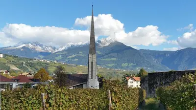 a church steeple in a village with mountains in the background at Ferienwohnung mit Garage, Fahrradraum und sehr großer sonnenverwöhnten Terrasse in Lagundo