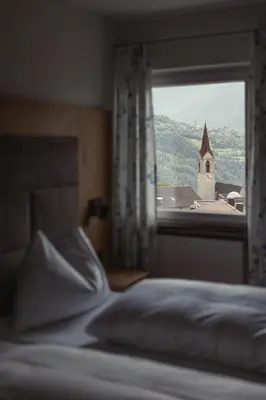 a bedroom with a bed and a window with a church at Hotel Oberwirt in Velturno
