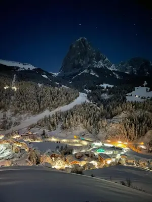 a town in the snow at night with a mountain at Pension Dolomieu in Santa Cristina in Val Gardena