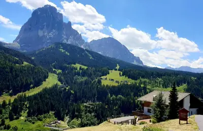 a house on a hill with mountains in the background at Pension Dolomieu in Santa Cristina in Val Gardena