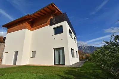 a white house with a roof on a green yard at Casa Alpina in Cavalese
