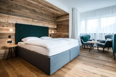 a bedroom with a bed and two chairs and a table at Hotel Ciasa Tamá in La Villa