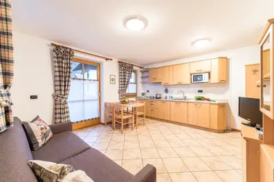 a living room with a couch and a kitchen at Cèsa Bel Seren in Campitello di Fassa