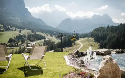 two chairs sitting on the grass next to a river at Surega - Idyllic Farmhouse in San Cassiano