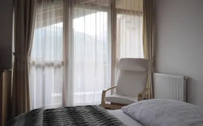 a bedroom with a chair and a bed and a window at Apartments Etruska in Santa Cristina in Val Gardena
