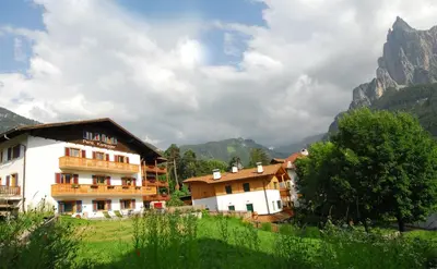 a building on a hill with mountains in the background at Garni Karlegger in Siusi