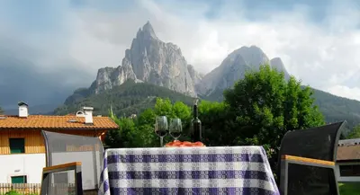 a table with wine glasses and a table with mountains in the background at Garni Karlegger in Siusi