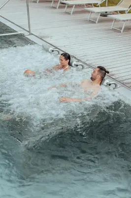 two people in a jacuzzi in a swimming pool at Biohotel theiner's garten in Lana