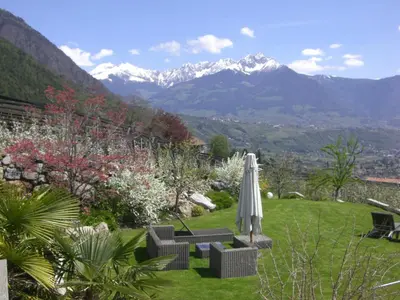 a patio with an umbrella and chairs and mountains at Residence BADLEIT in Lagundo