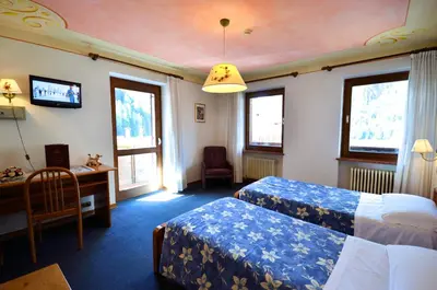 a hotel room with two beds and a desk and windows at Hotel Centrale in Alleghe