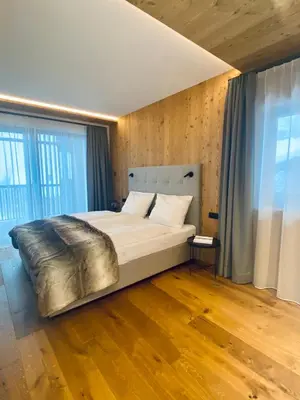 a large bed in a room with wooden floors and windows at Florisa Mountain Penthouse in San Vigilio Di Marebbe