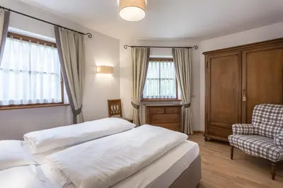 a bedroom with two beds and a chair and windows at Residence Castel in Ortisei