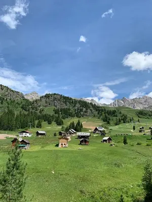 a green field with a group of houses in a mountain at Appartamento San Pellegrino in Passo San Pellegrino