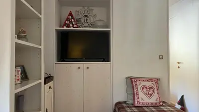 a living room with a tv and a cabinet and a chair at Appartamento San Pellegrino in Passo San Pellegrino