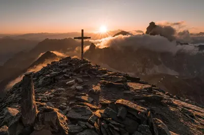 a cross on the top of a mountain at sunset at Apartments Ban Guggugg in Colle Isarco