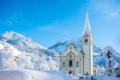 a church in the snow with mountains in the background at San Vigilio di Marebbe - Suite di Montagna in San Vigilio Di Marebbe