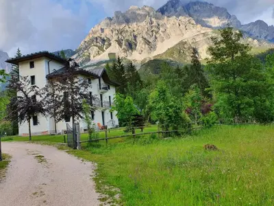 a house in a field with a mountain in the background at Mansarda 4 posti letto in Villa a Borca di Cadore in Villanova