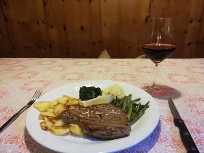 a plate of steak and vegetables with a glass of wine at Gasthof Thaler in Mezzaselva