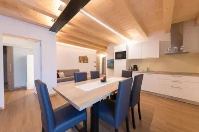 a kitchen and dining room with a wooden table and blue chairs at Latemar Fiemme Apartments in Tesero