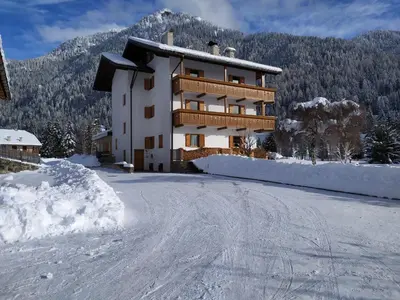a building on a snow covered road with a mountain at Residence Colibrì in Pozza di Fassa