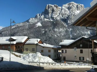 a snow covered mountain in front of a town with buildings at La casa! in Vigo di Fassa