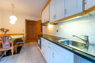 a kitchen with white cabinets and a sink and a table at Apartment Belvedere in Selva di Val Gardena