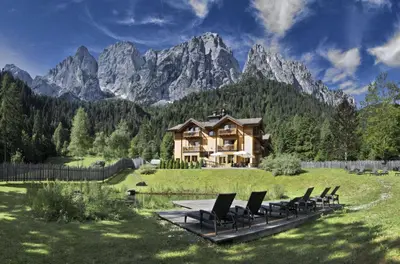 a house on a field with chairs and mountains at Hotel Chalet Giasenei in Sagron Mis