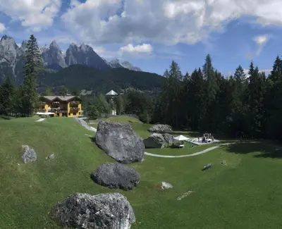 a green field with large rocks in front of a house at Hotel Chalet Giasenei in Sagron Mis