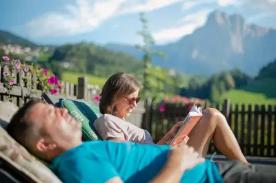 a man and a woman laying on a couch reading books at Nuierhof in Castelrotto