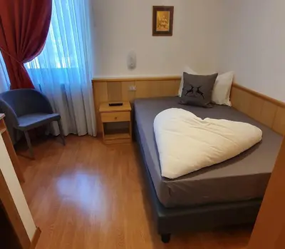 a small bedroom with a bed and a chair at Albergo Dolomiti in Cavalese