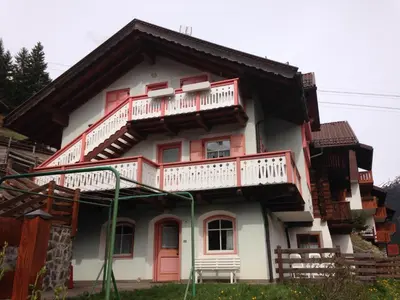 a house with red doors and a balcony at Appartamento Col Val di Fassa con giardino BAGNI RINNOVATI 2023 in Campitello di Fassa