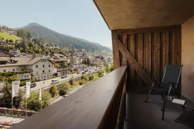 a bedroom with a bed and a chair and a balcony at Hotel COSMEA 4 Stars - Your Dolomites experience in Ortisei
