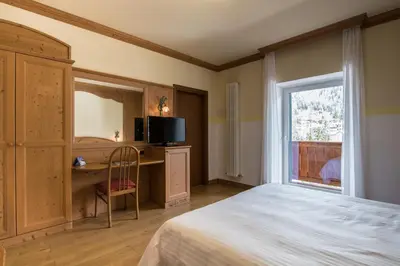 a bedroom with a bed and a desk and a window at Hotel Colfosco in San Martino di Castrozza
