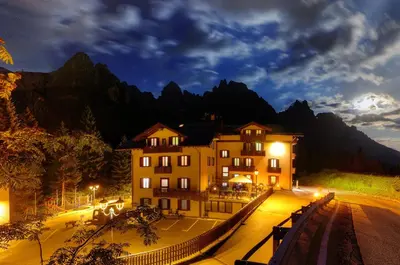 a building on a street at night with mountains at GH Hotel Fratazza in San Martino di Castrozza