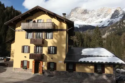 a yellow building with a balcony and snowy mountains at GH Hotel Fratazza in San Martino di Castrozza