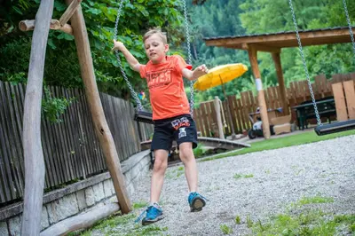 a young boy is playing on a swing at Hotel Sigmunderhof in Chienes
