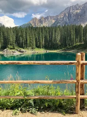 a wooden fence next to a lake with mountains at NRH Laurin Karersee in Nova Levante
