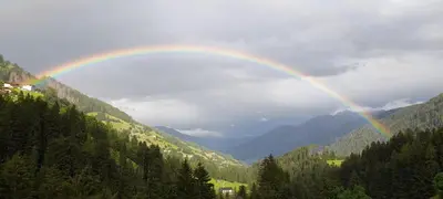 a rainbow in the sky over a valley with trees at Ober-Gruberhof in Ridanna