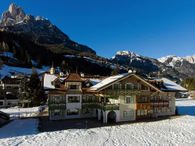 a building in the snow with mountains in the background at Residence Holiday in Pozza di Fassa
