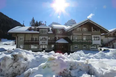 a building covered in snow with the sun behind it at Residence Holiday in Pozza di Fassa