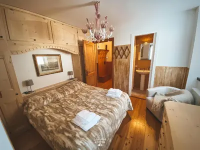a bedroom with a large bed and a chandelier at Una Perla a Cortina in Cortina dʼAmpezzo