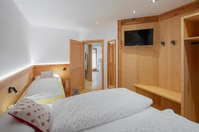 a bedroom with two beds and a tv on the wall at Cesa La Doe Majons in Campitello di Fassa