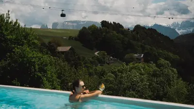 a woman in a swimming pool with mountains in the background at Pippos Mountain Lodge in Soprabolzano