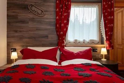 a bedroom with a red bed with red pillows and a window at B&B Cesa Marlen in Canazei