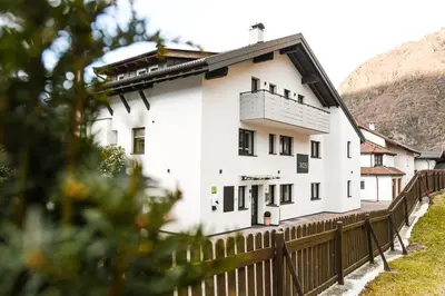 a white building with a fence and mountains in the background at byRosi Apartments in Parcines