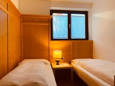 two beds in a small room with a window at Appartamenti Pichler in Castello di Fiemme