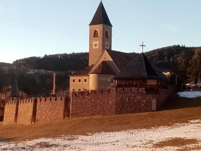 a church with a clock tower and a wall at Siusi Sciliar Apartment in Siusi