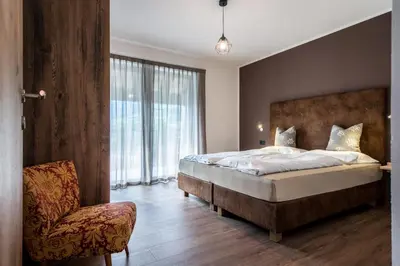 a bedroom with a large bed and a chair at Chalet Kristall - Dolomites Garden Chalet in Falzes